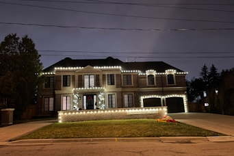 Christmas light installation Etobicoke with bright holiday lights on the roofline, garage doors, entrance door and exterior wall of a two story home